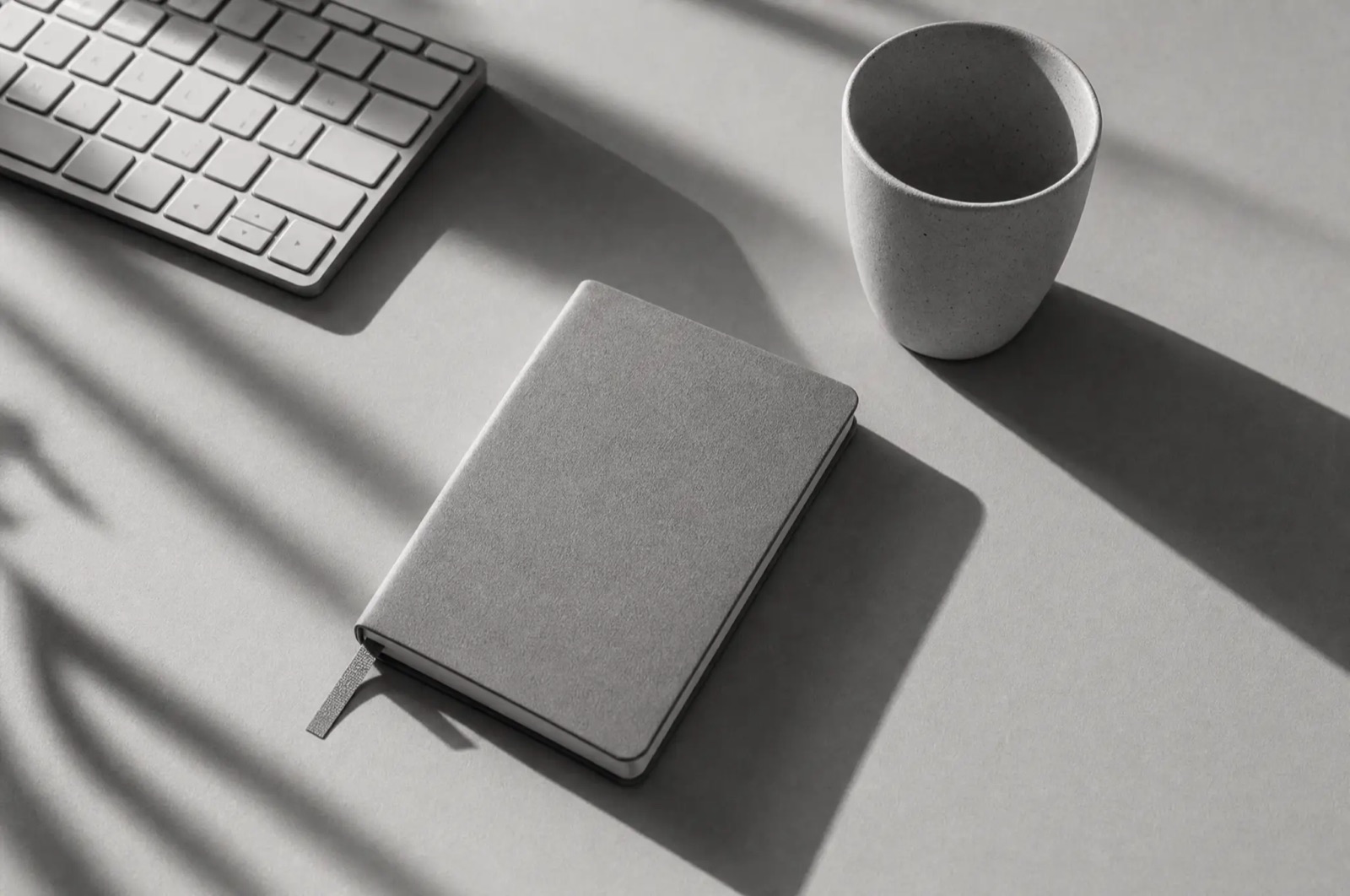 Minimal desk scene with keyboard, notebook, and a cup
